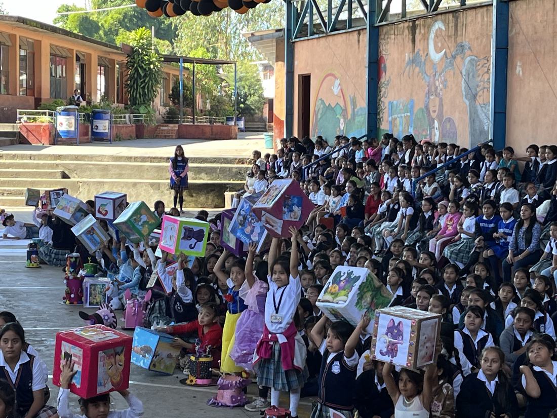 Students holding decorated book-box costumes overhead at Felipa Gómez school
